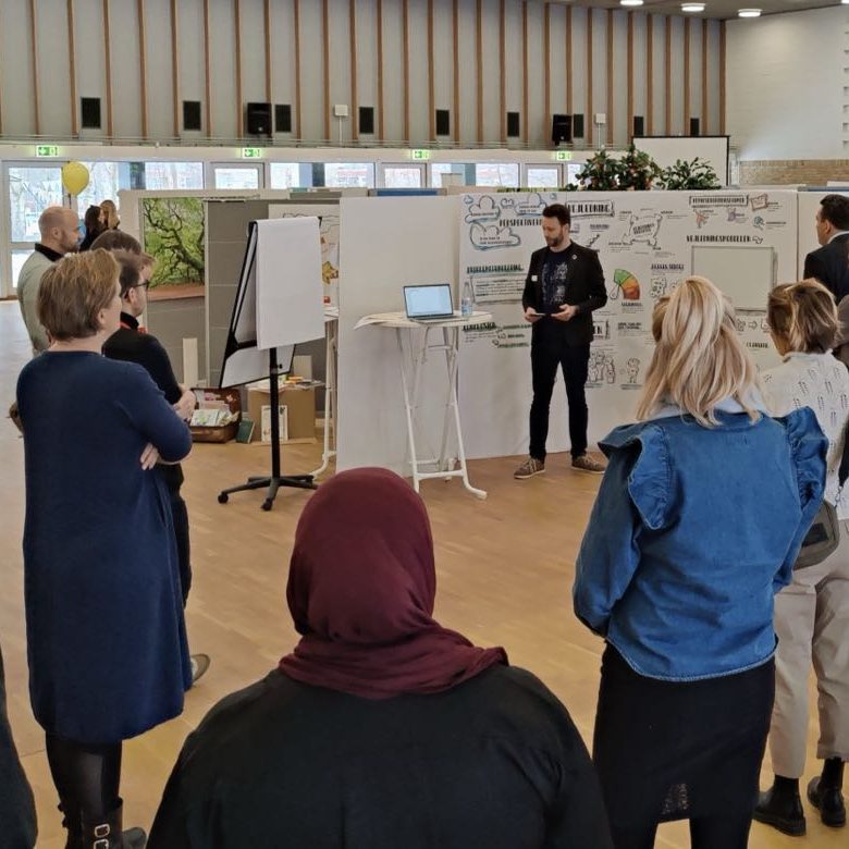 Lærere og pædagoger ved en scene, hvor de præsenterer deres eksamen for publikum