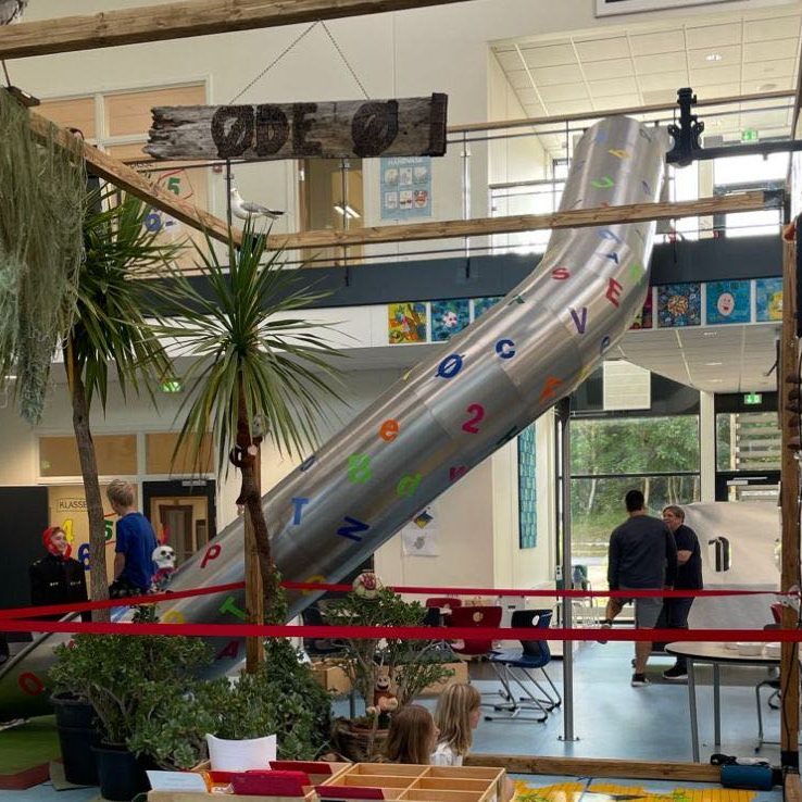 Et stort lokale på en skole, der er indrettet med rutschebane og forskellige stationer med teknologi og materialer, som kan bruges til at inddrage legen i undervisningen